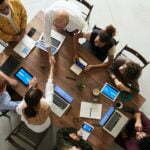 a group of people sitting around a table with laptops
