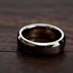 a close-up of a sleek tungsten carbide ring resting on a dark, polished wooden surface.